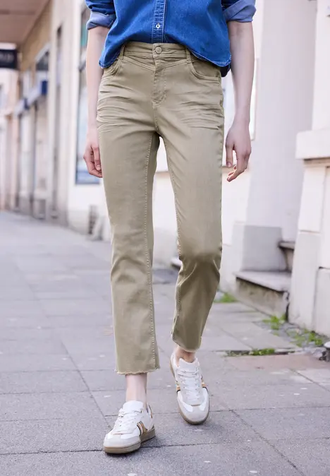 Een persoon loopt op het trottoir met een blauwe blouse, beige broek en witte sneakers.