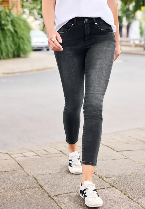 Een persoon draagt zwarte skinny jeans en witte sneakers op een stoep.