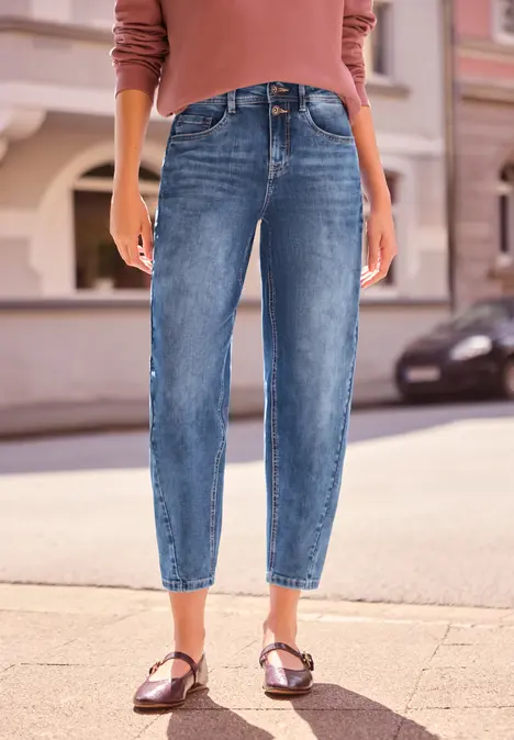 Eine Person steht auf dem Bürgersteig und trägt lässige blaue Jeans und braune Sandalen.