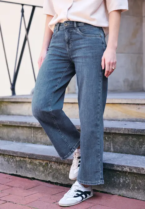 Person steht auf einer Treppe, trägt blaue Jeans mit weitem Bein und weiße Sneaker.