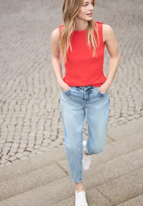 Een vrouw in rood topje, blauwe jeans en witte sneakers loopt een geplaveide trap af.