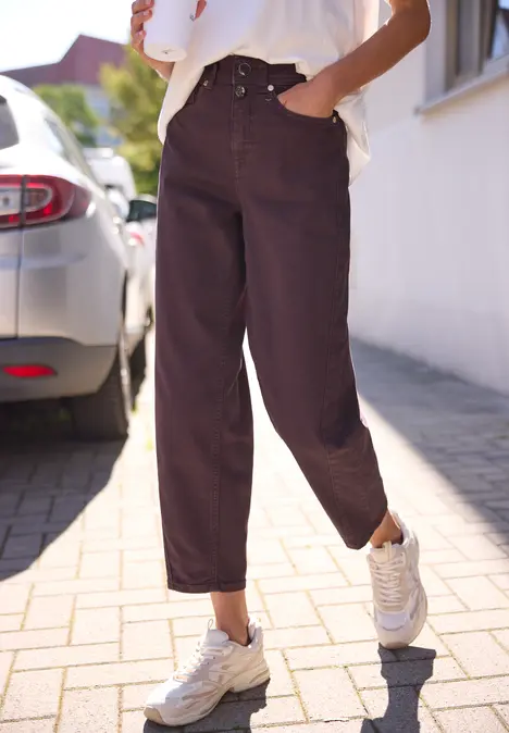 Person trägt weite, dunkle Jeans und weiße Sneaker, steht auf dem Gehweg neben einem Auto.