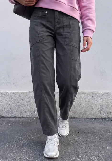 Iemand loopt over het trottoir, draagt donkergrijze broeken, witte sneakers en een roze trui.