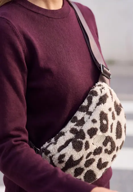 Une personne porte un pull bordeaux et un sac bandoulière à imprimé léopard.